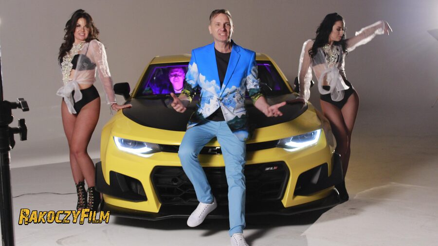 Plan zdjęciowy teledysku: Robert Sasinowski w błękitnej marynarce siedzi na masce żółtego Chevroleta Camaro, obok dwie tancerki
